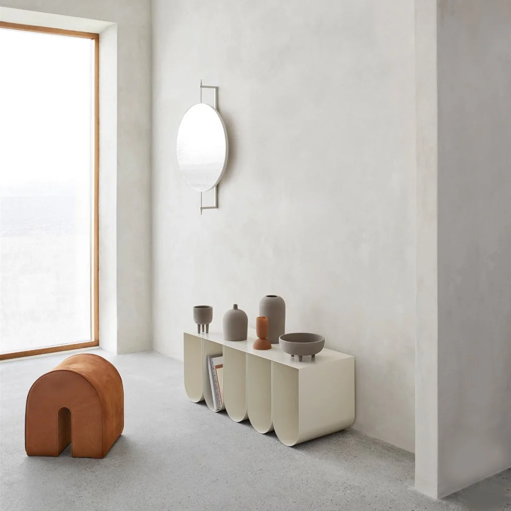 Minimal interior with a sculptural wall light, pale sideboard and terracotta stool.