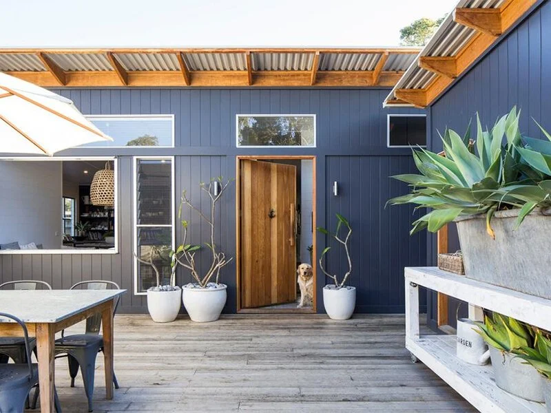 Timber courtyard deck with dark cladding, dining furniture and planted pots.