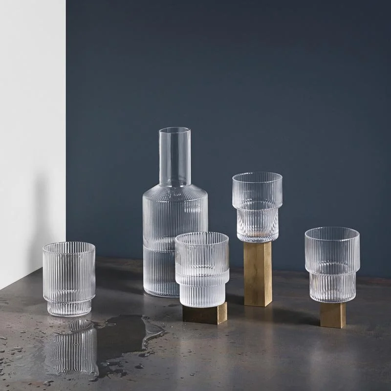 Clear glass carafe and glasses with brass-toned bases on a dark stone surface.