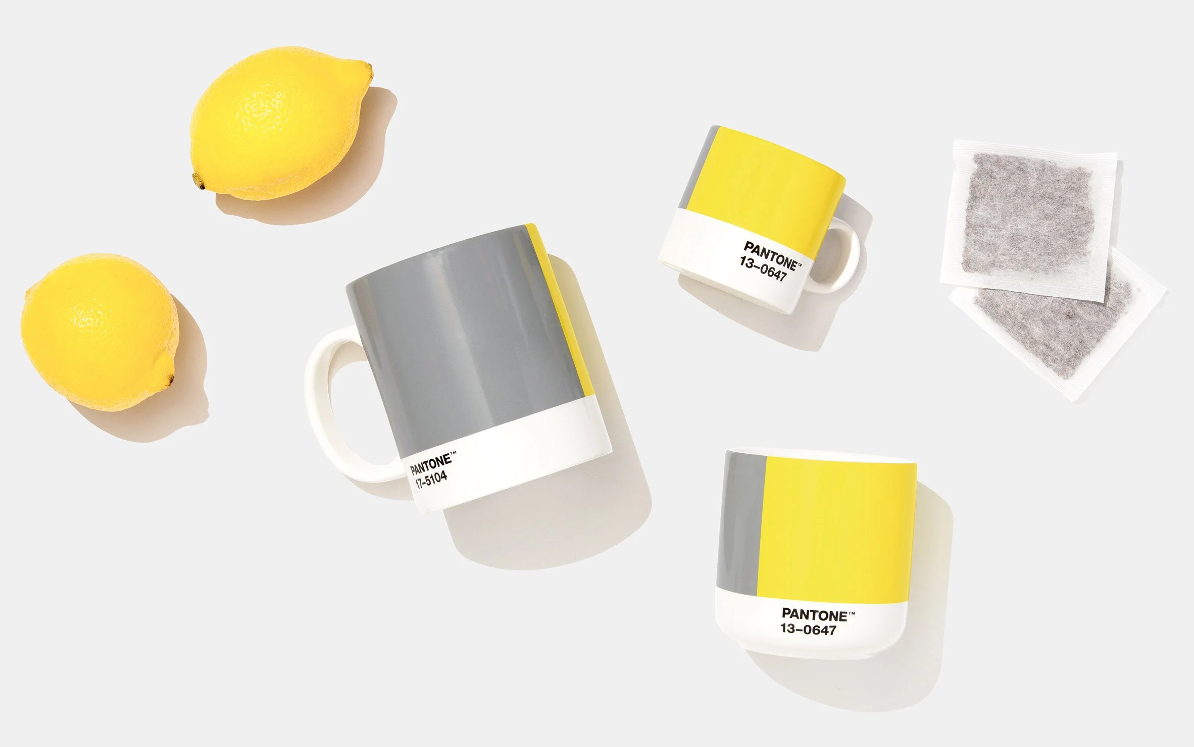 Grey and yellow mugs arranged with lemons on a pale background.
