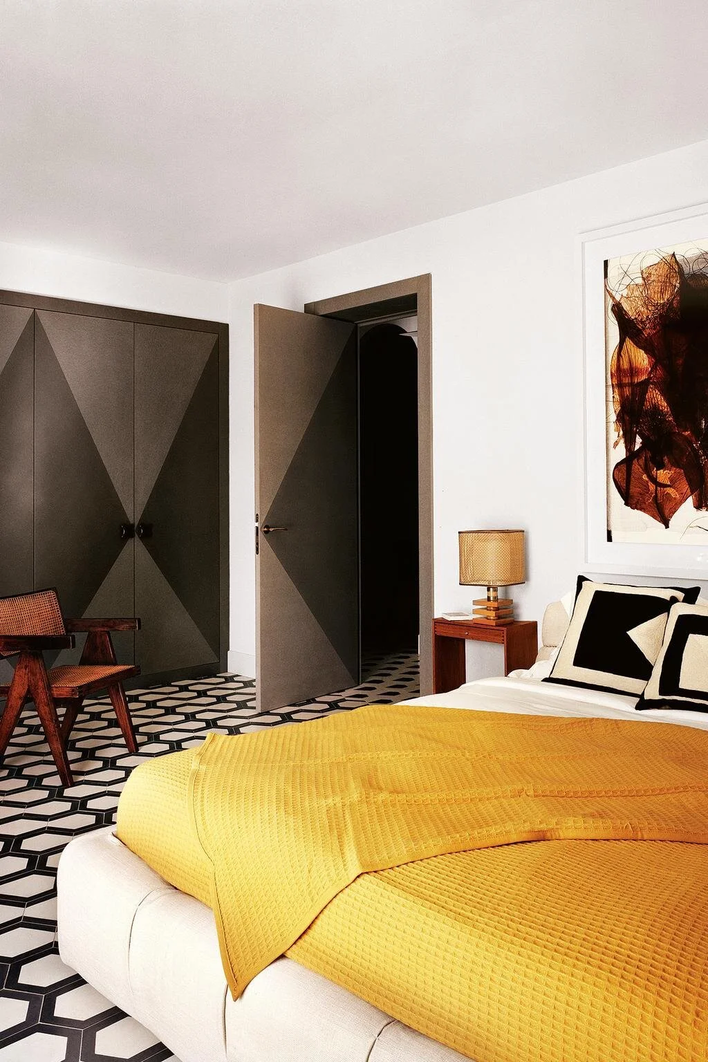 Yellow bed linen in a bedroom with a patterned floor and dark geometric doors.