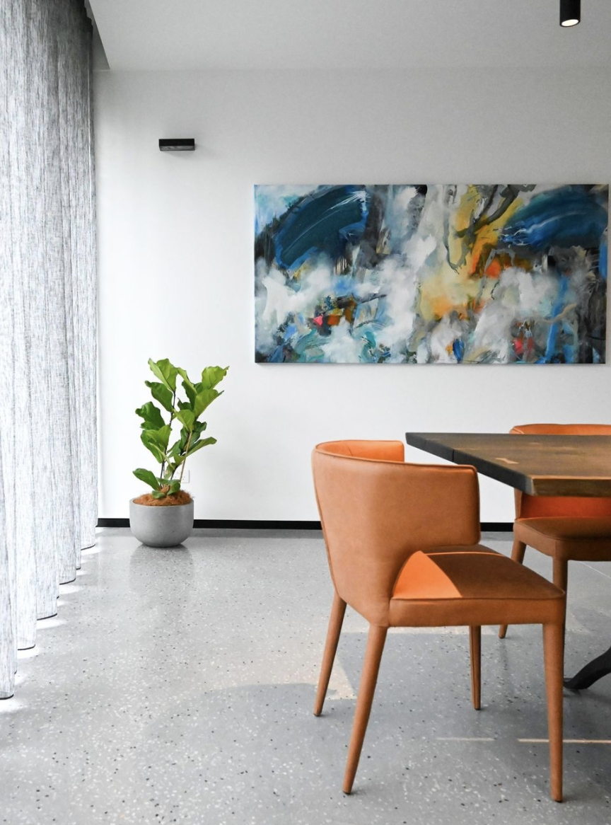 Orange upholstered dining chairs beside sheer curtains and a colourful abstract artwork.