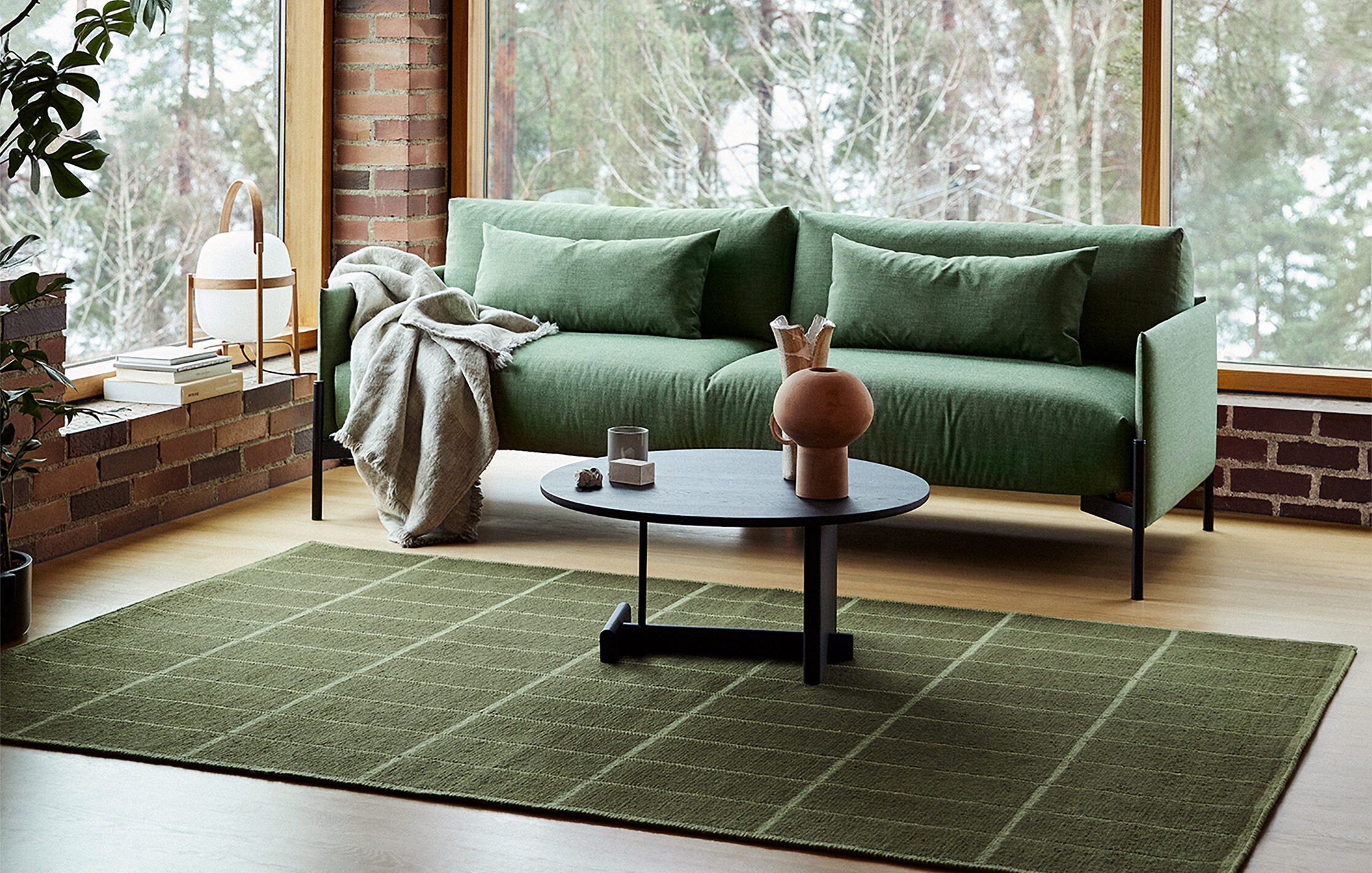 Green sofa and round coffee table beside tall windows and exposed brickwork.