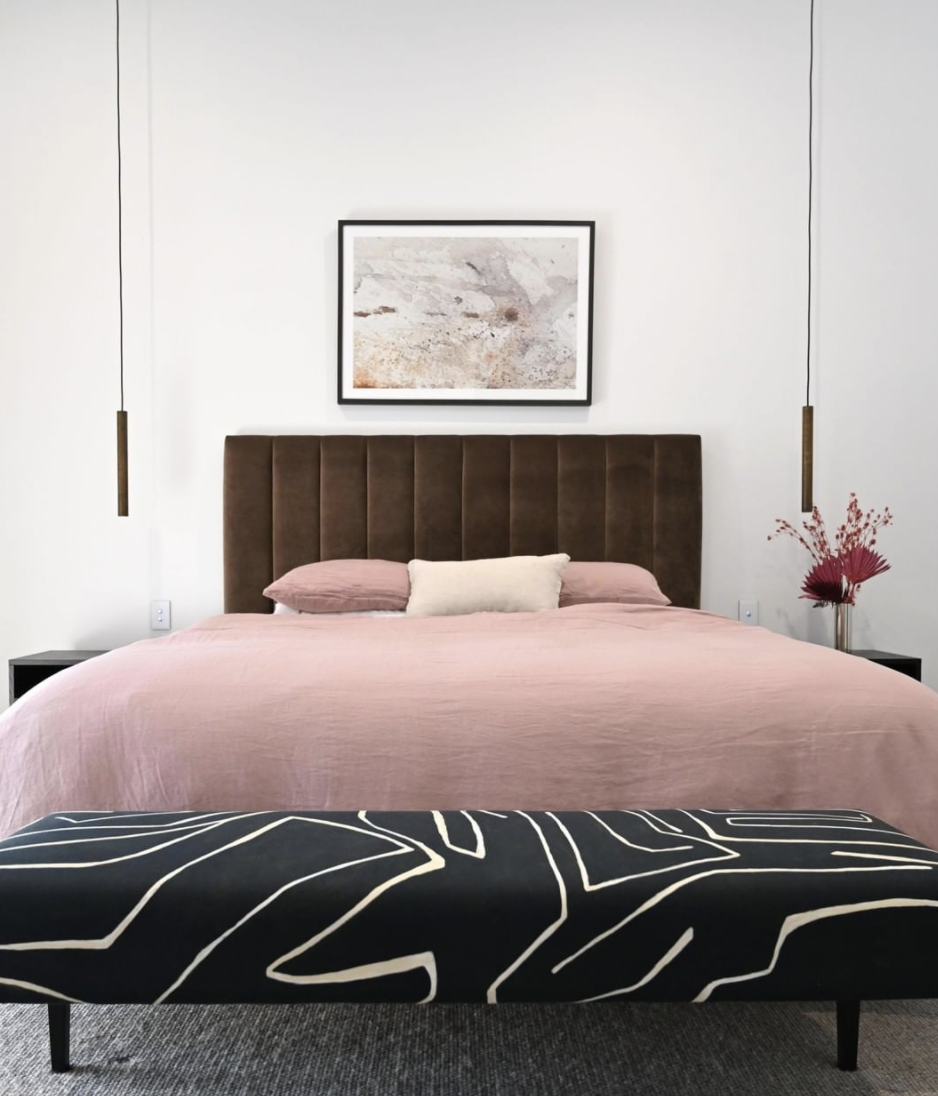 Pink bed linen against a dark channelled bedhead with suspended bedside lights.