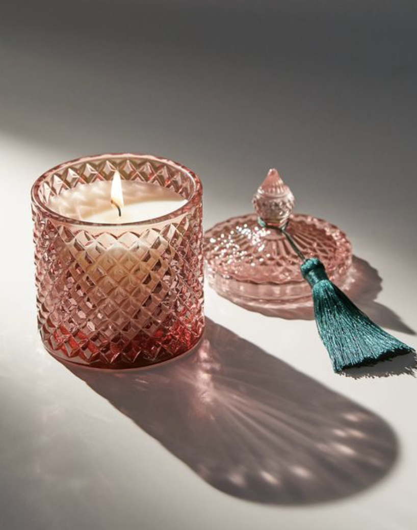 Pink cut-glass candle vessel and matching lid with decorative tassels.