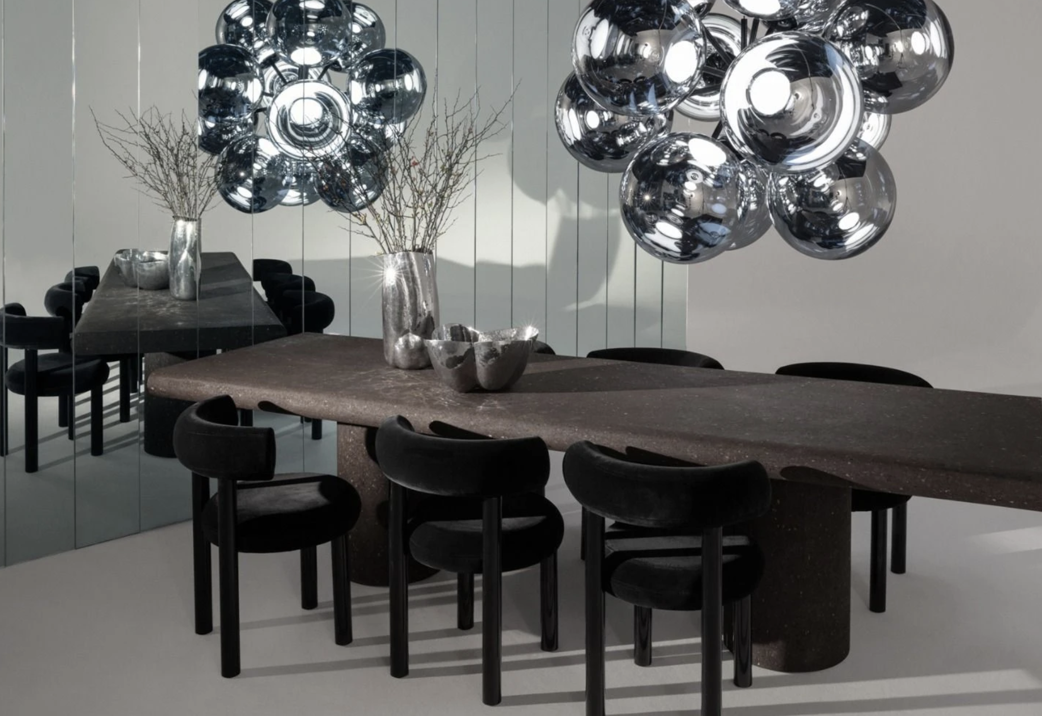 Reflective sculptural pendant lights above a dark dining table and chairs.