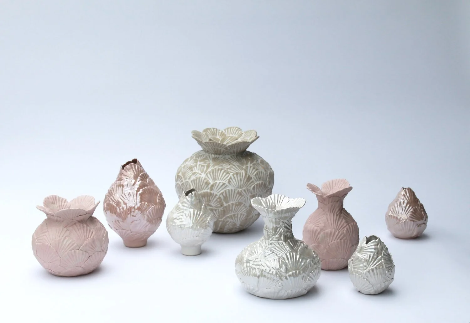 Collection of hand-built ceramic vessels in soft pink and pale green tones.