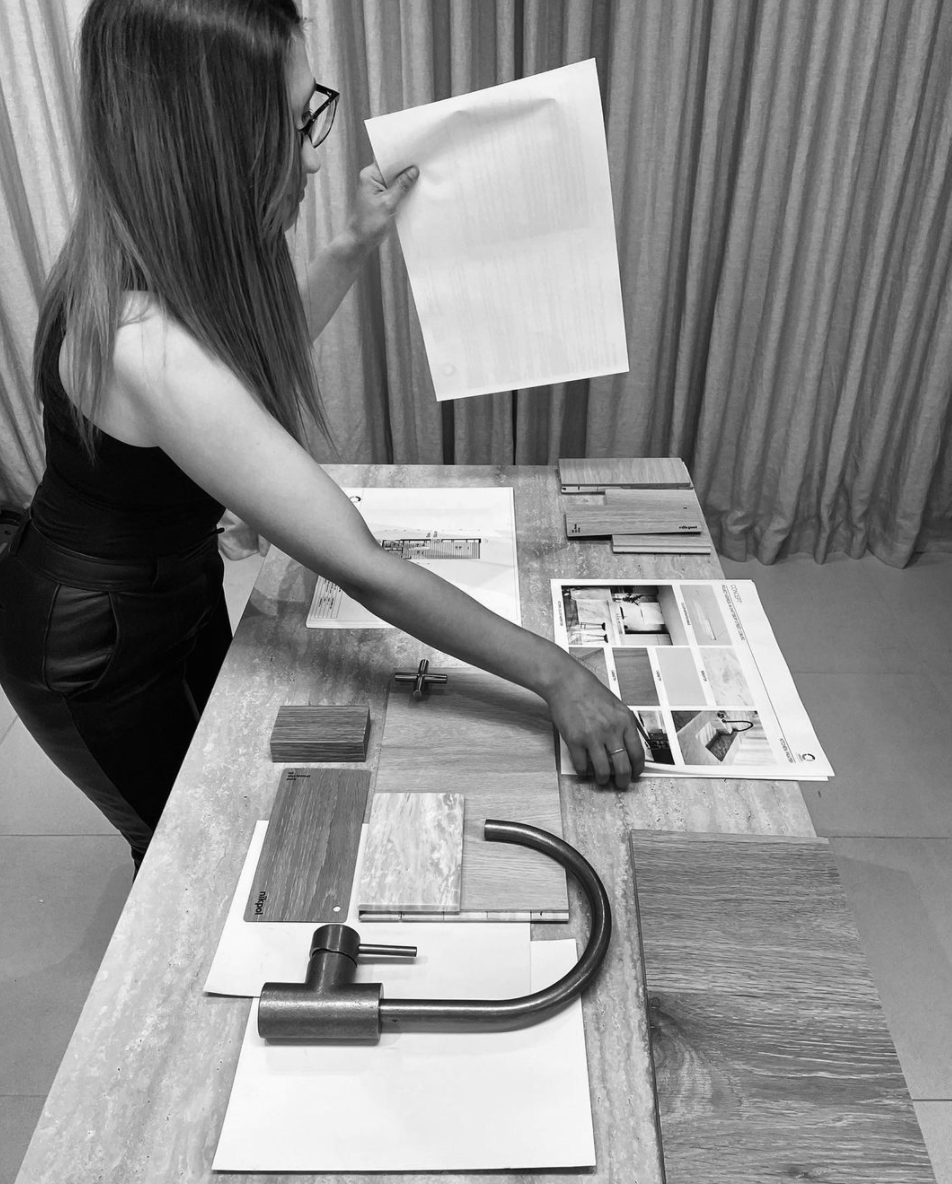 Designer reviewing plans and materials at a workbench in a black-and-white photograph.