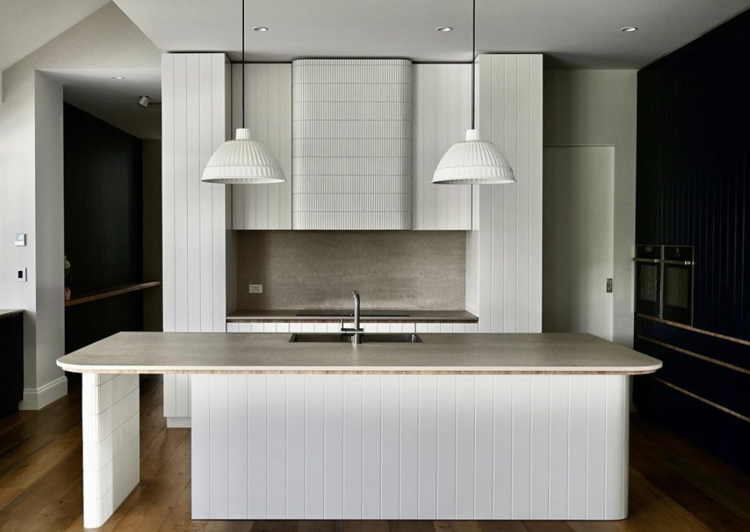 Kitchen with a pale island, vertical panelling and paired pendant lights.