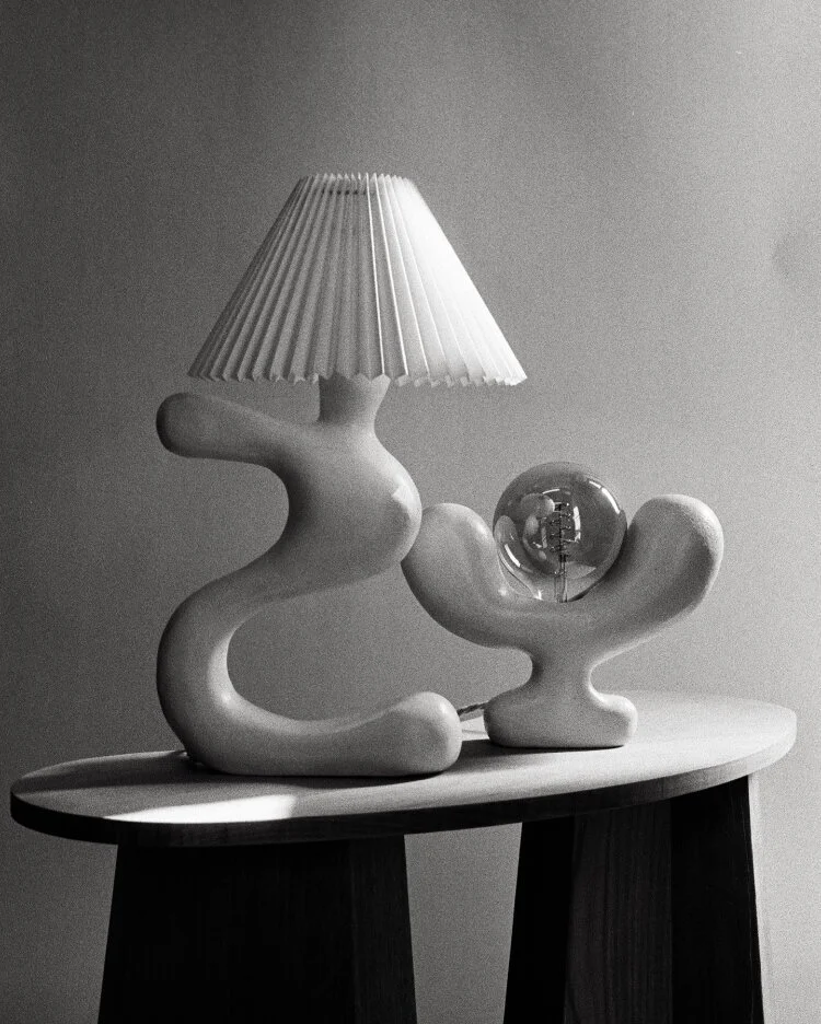 Sculptural ceramic lamp and vessel on a round dark table in a monochrome photograph.