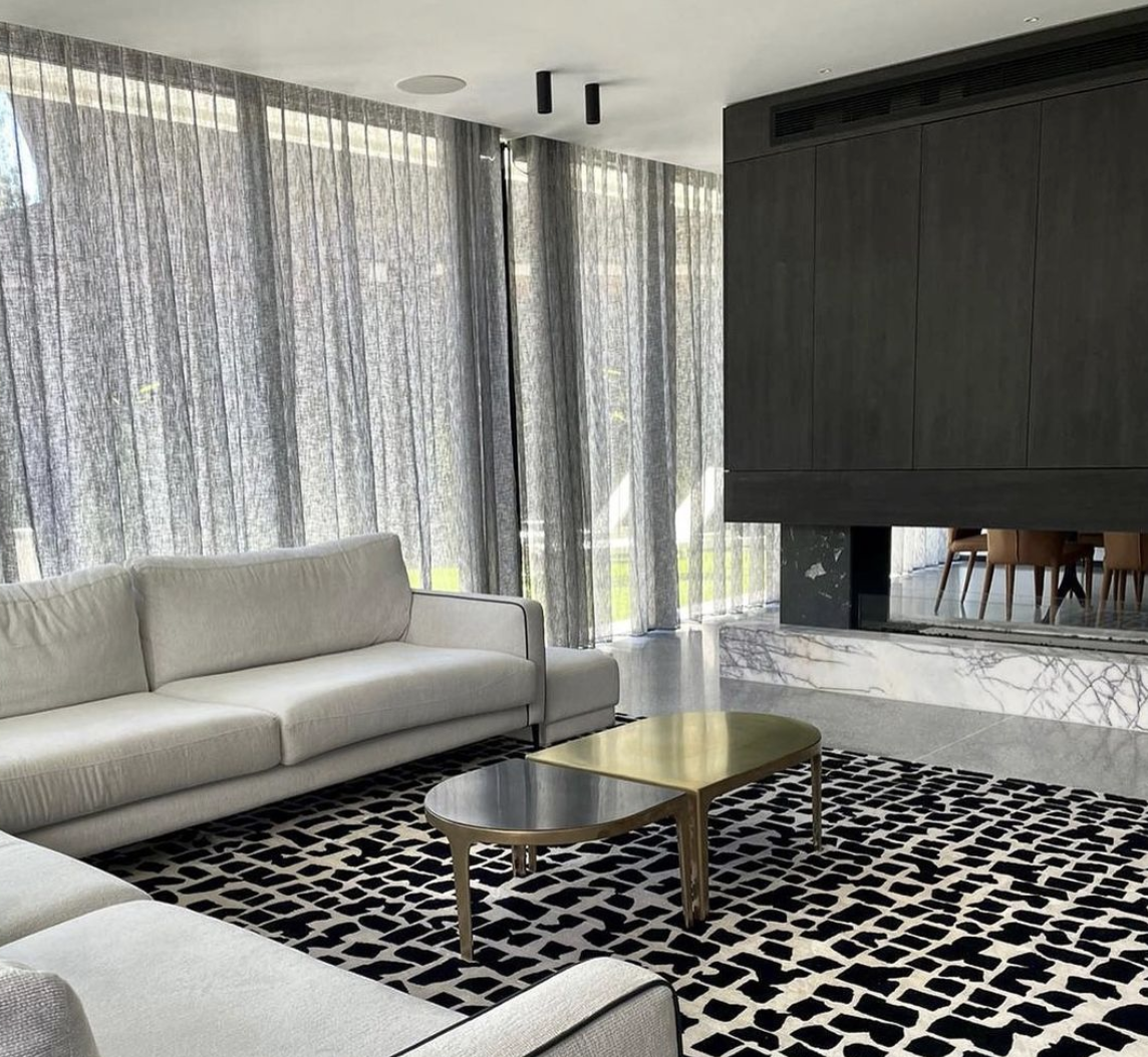 Pale sofa and coffee table beside sheer curtains and a dark fireplace.
