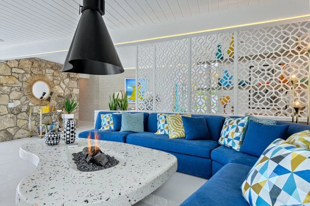 Blue seating and geometric cushions beside a pale terrazzo table and patterned room divider.