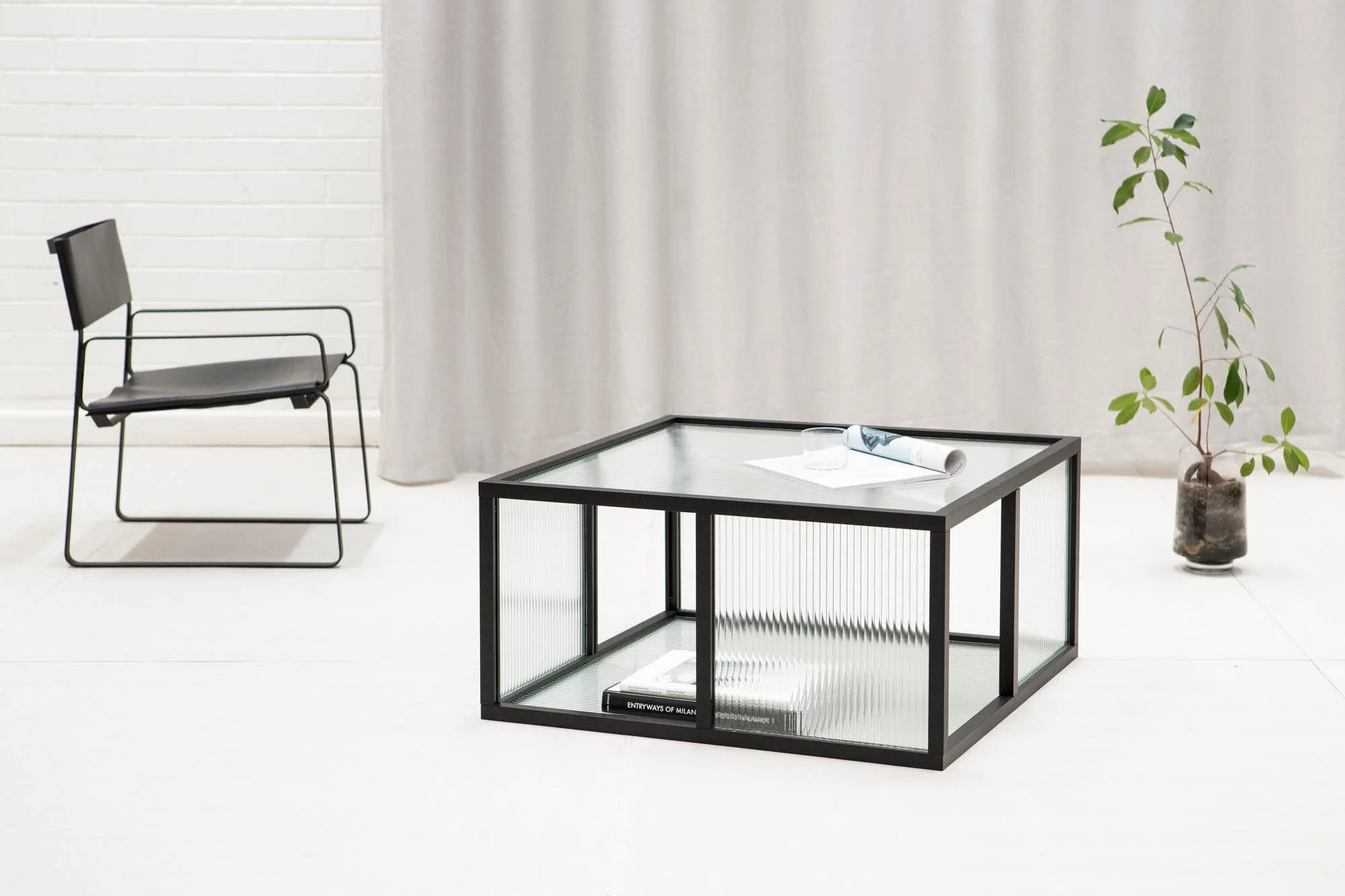 Black open-frame glass coffee table and black chair in a white interior.