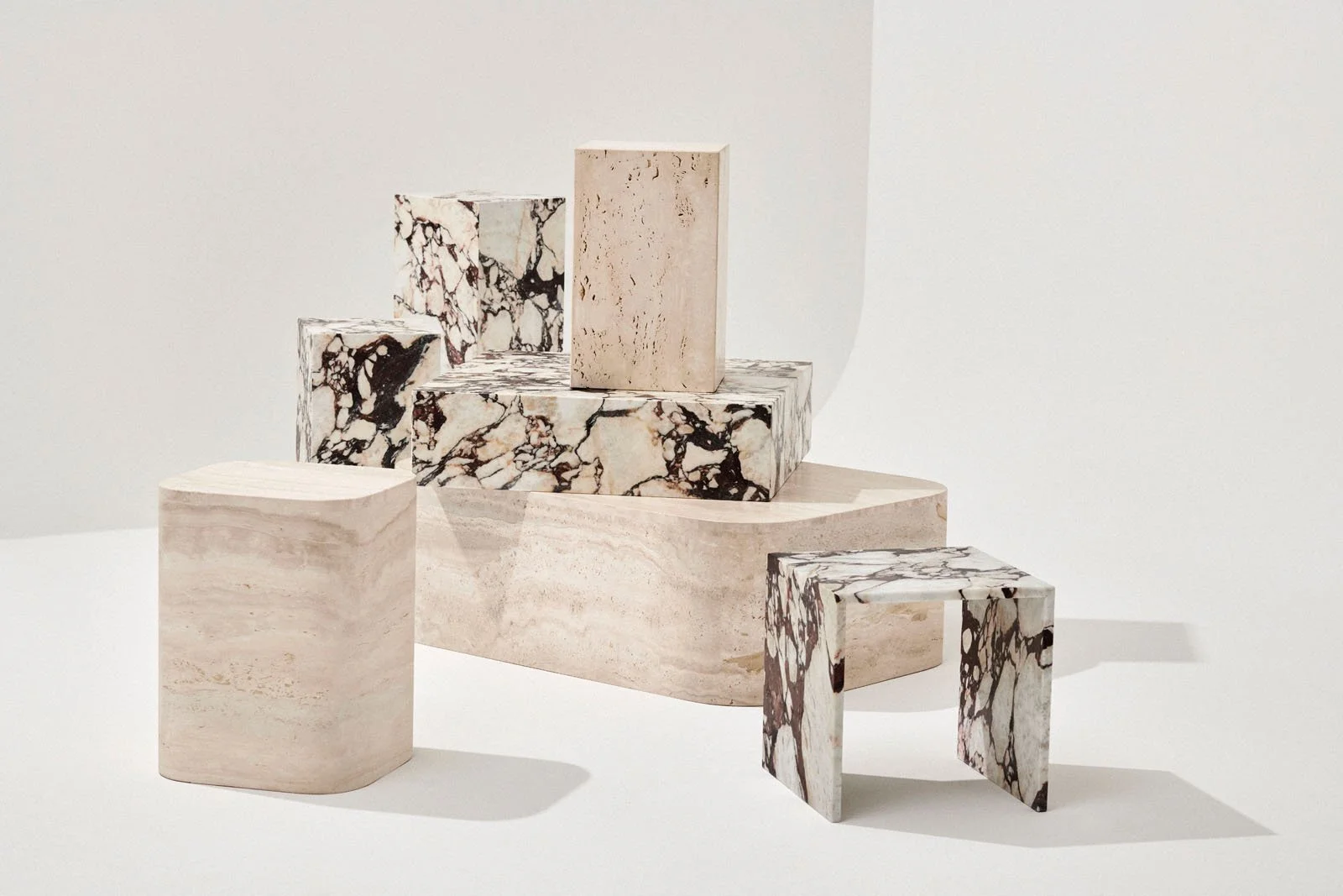 Sculptural natural stone stools, pedestals and blocks displayed against white.