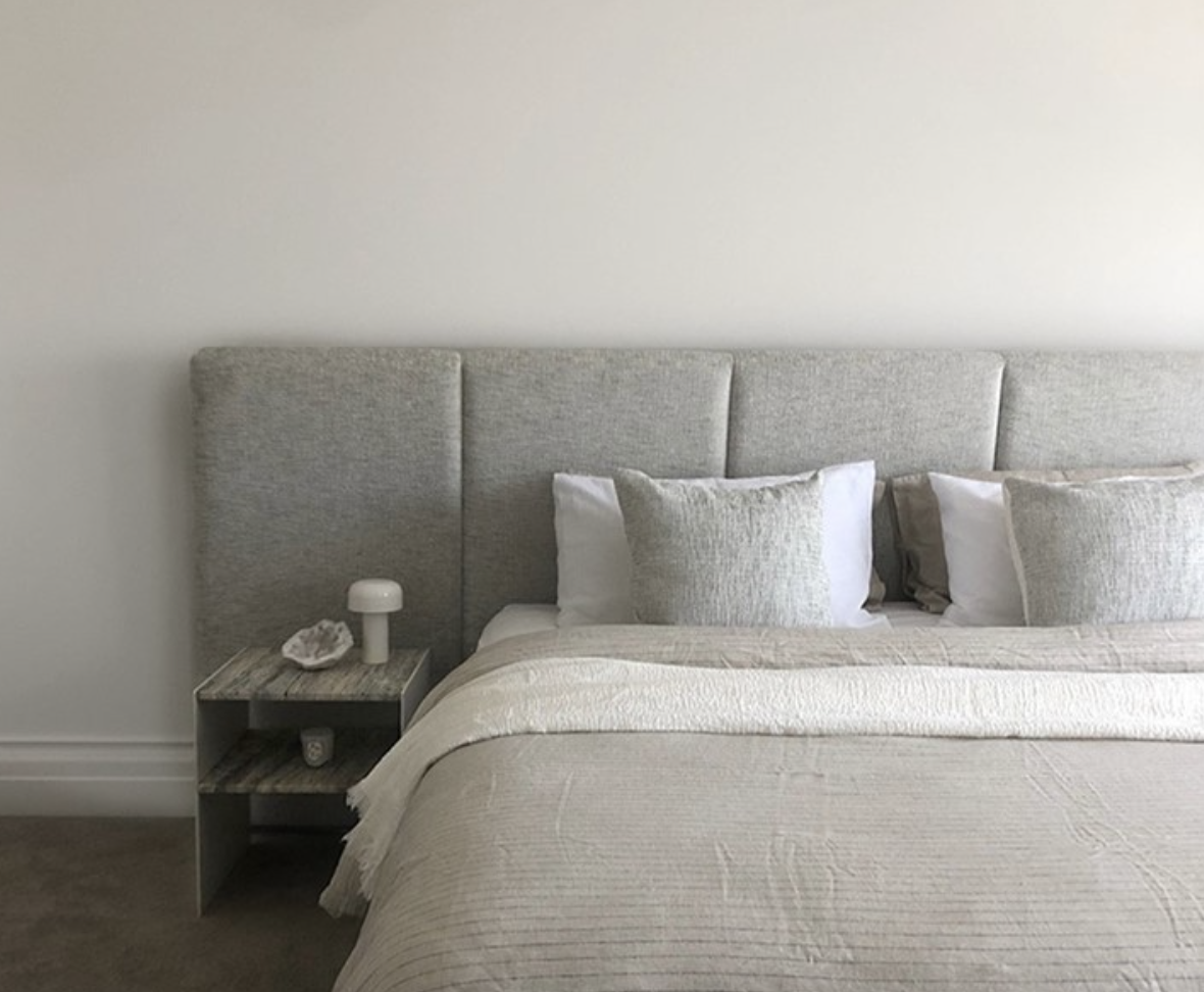 Pale bedding against a soft grey upholstered bedhead with a black bedside table.