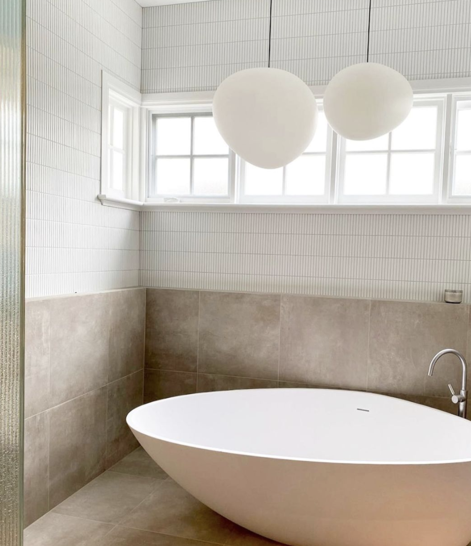 White freestanding bath against warm stone walls beneath two globe pendants.