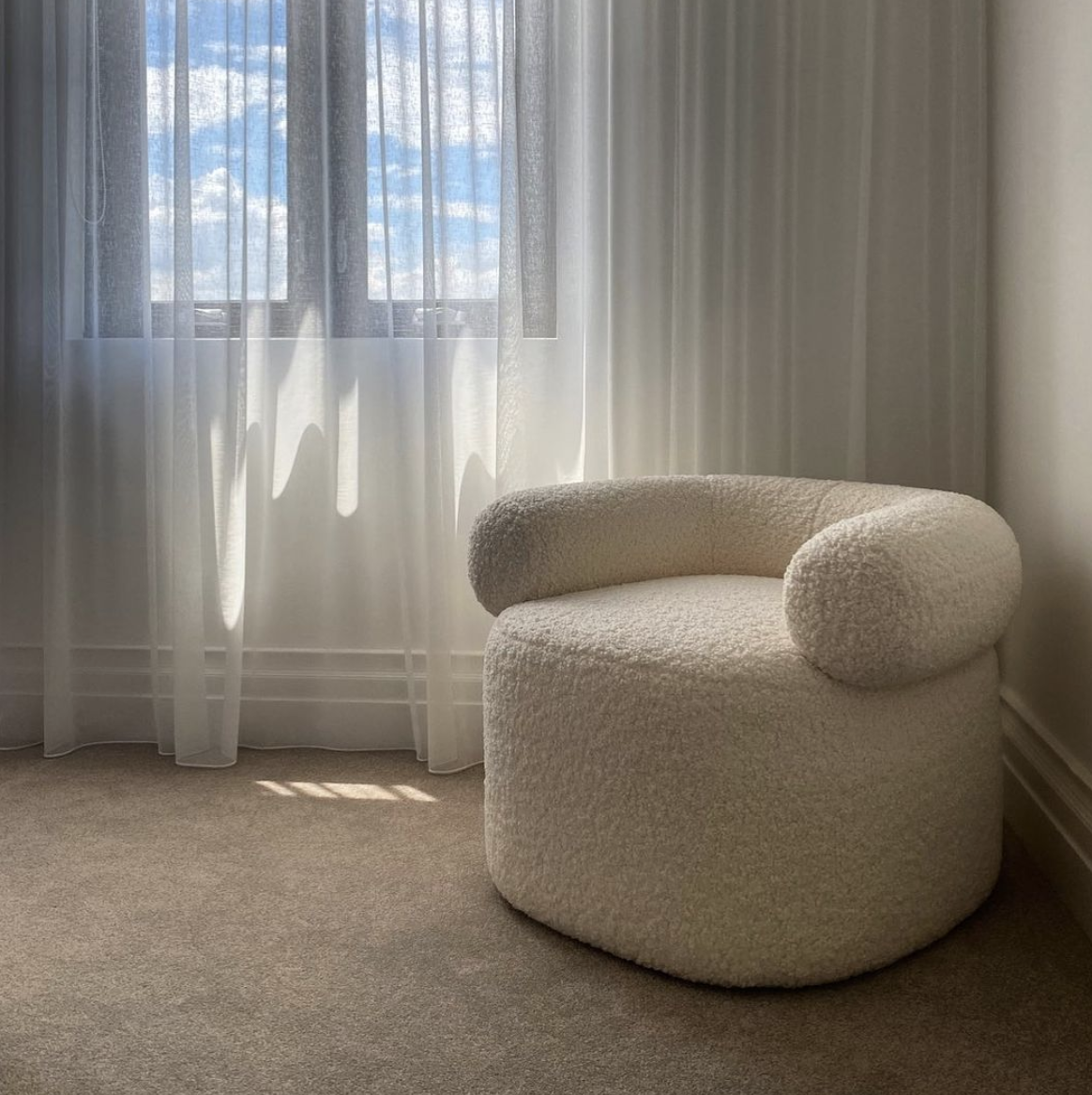 Cream boucle armchair beside softly lit sheer curtains.