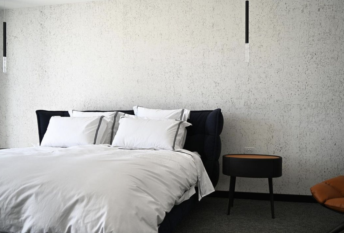 White bed linen and a dark curved bedhead against a textured light wall.