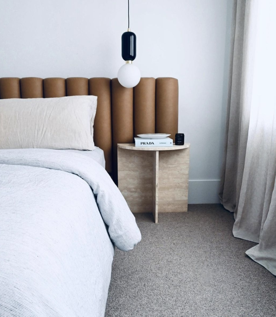Tan channelled bedhead with white linen and a pale bedside table.