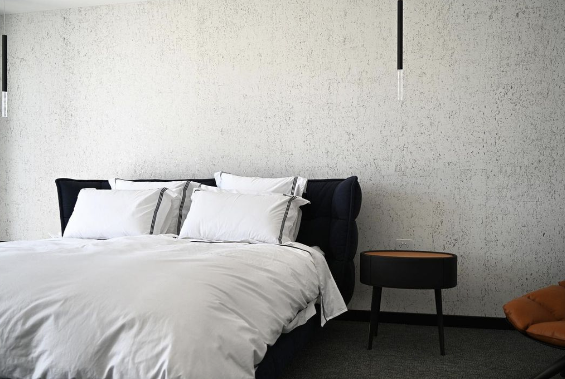 White bed linen against a dark curved bedhead beside a round timber table.