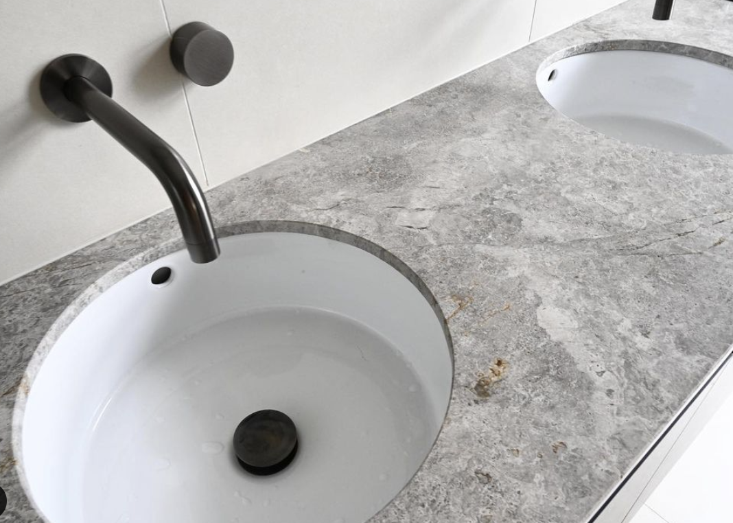 Pale stone vanity with a white basin and a curved black wall-mounted tap.