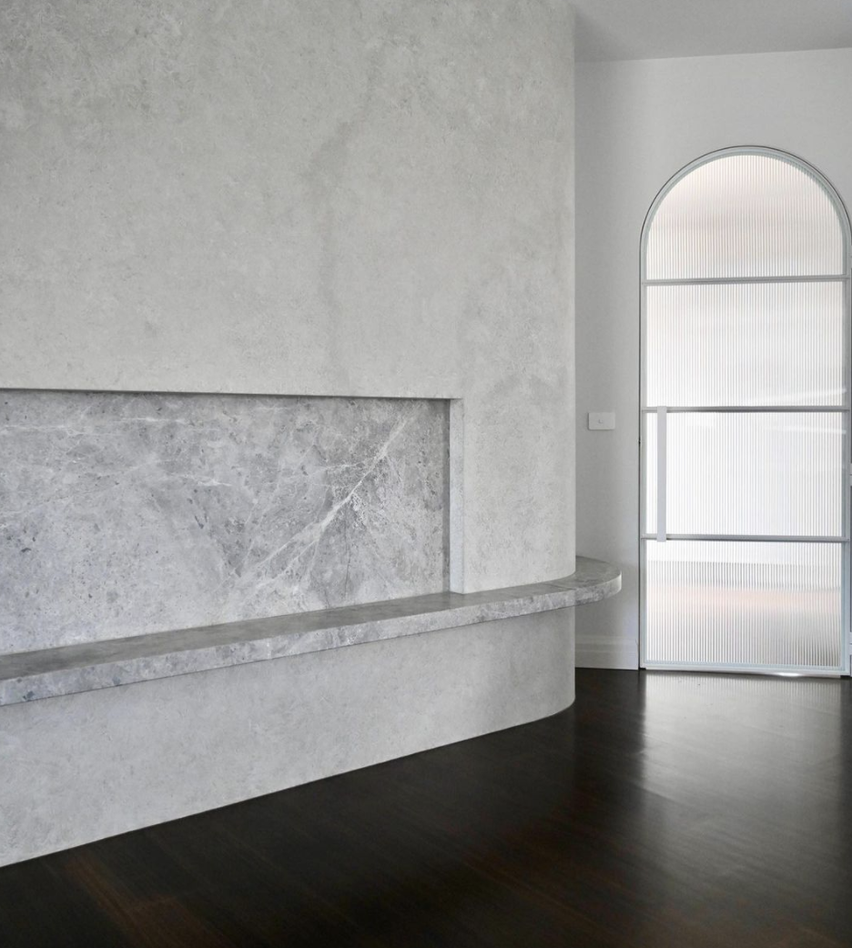 Pale stone fireplace beside an arched opening in a light-toned interior.