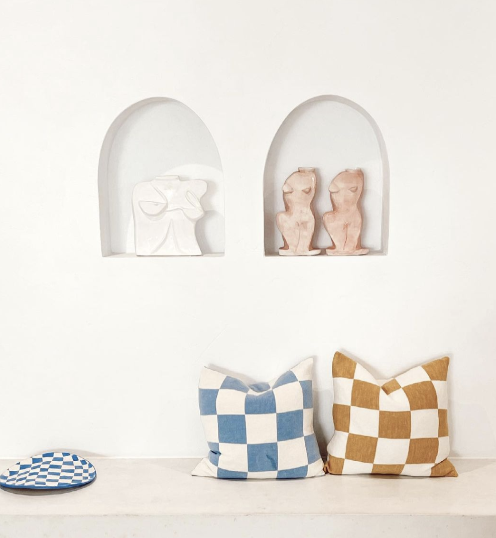 Paired arched wall recesses displaying small artworks above a bench with checked cushions.