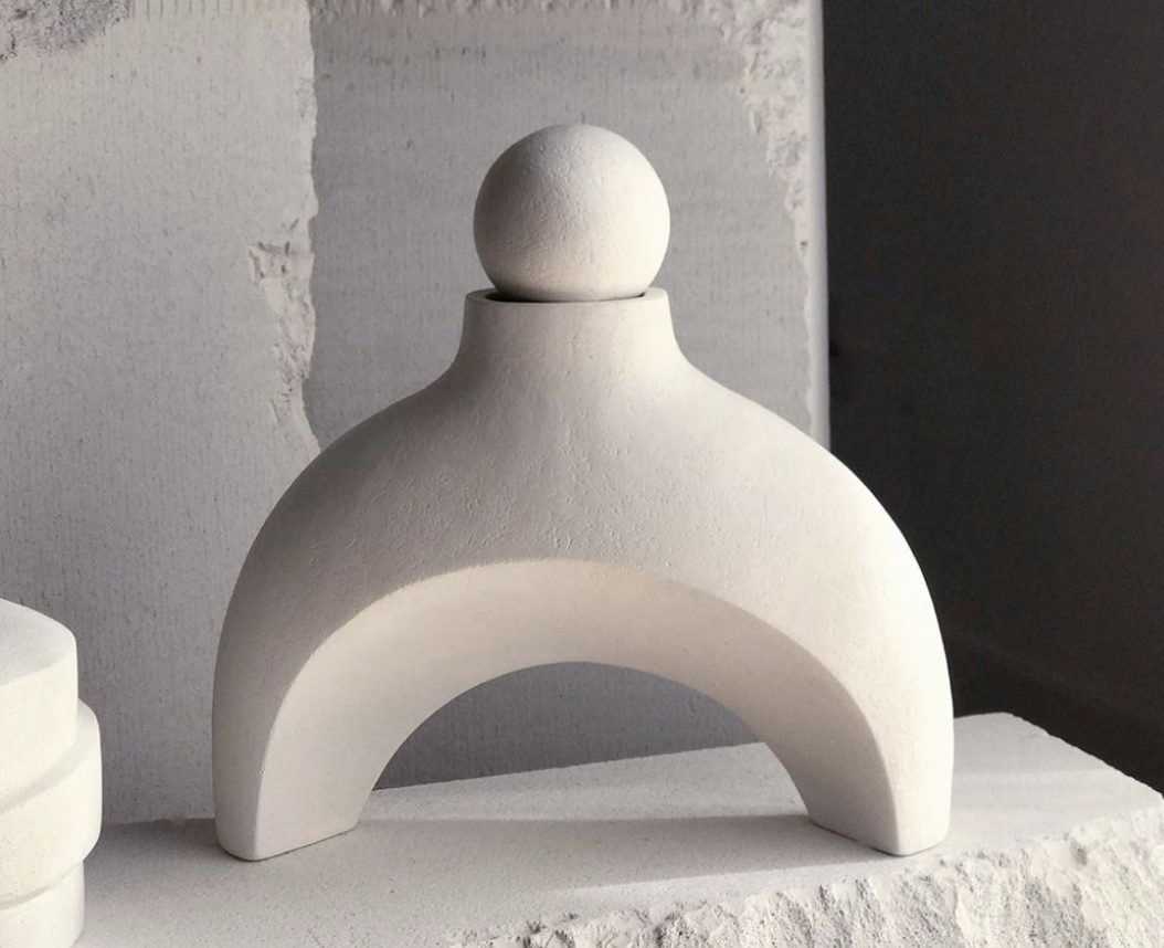 Pale ceramic object with an arched form and a rounded top.
