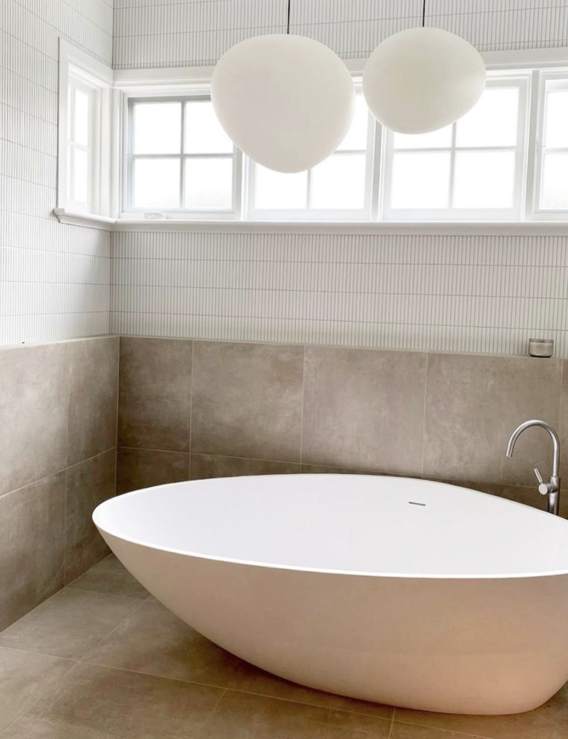 Freestanding white oval bath against warm stone walls beneath two globe pendant lights.