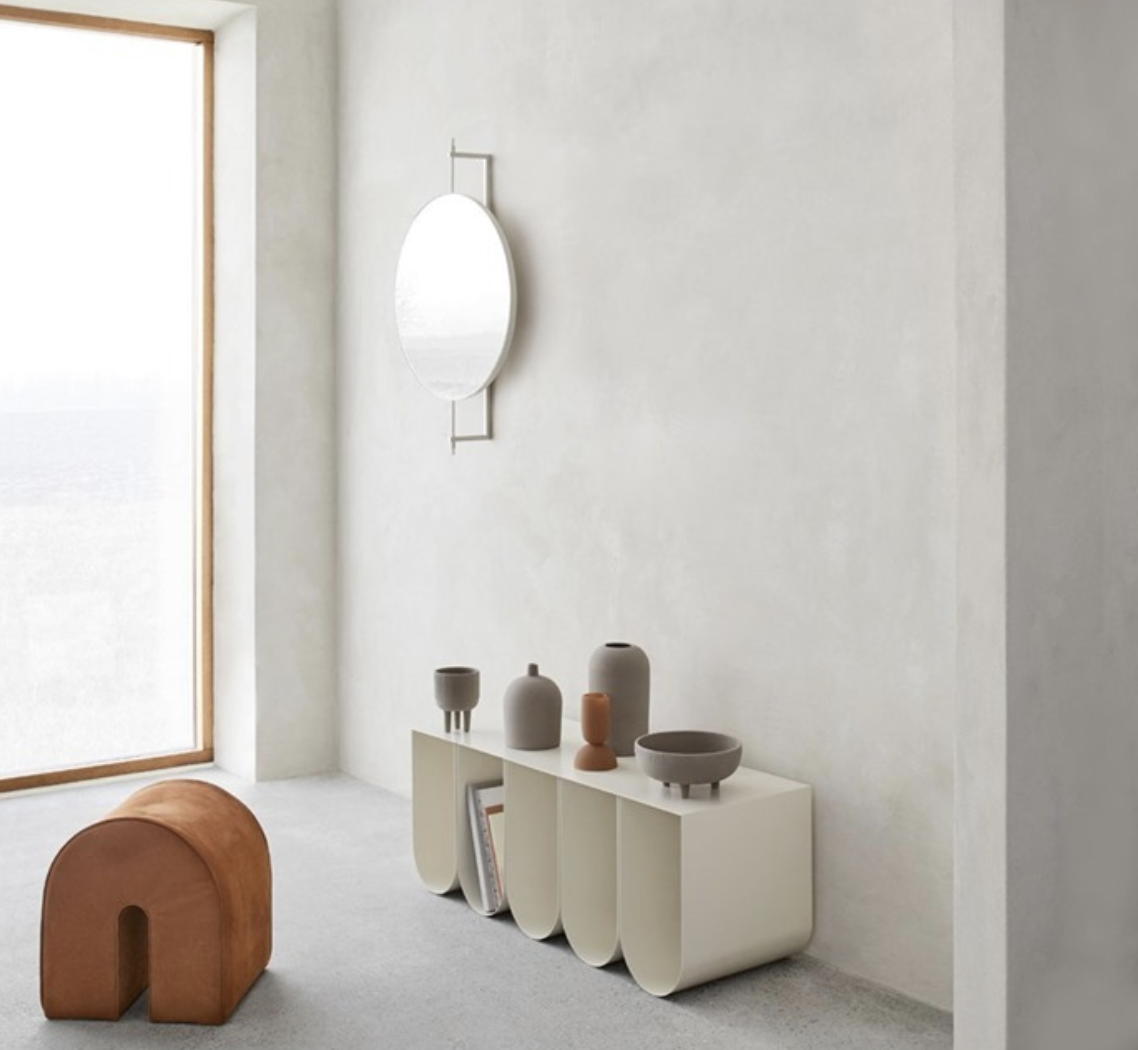 Sculptural cream cabinet and terracotta stool beneath an organic mirror beside a bright window.