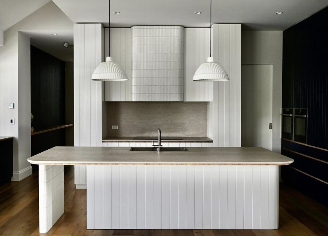 Kitchen island with a rounded stone end, vertical panelling and two pendant lights.