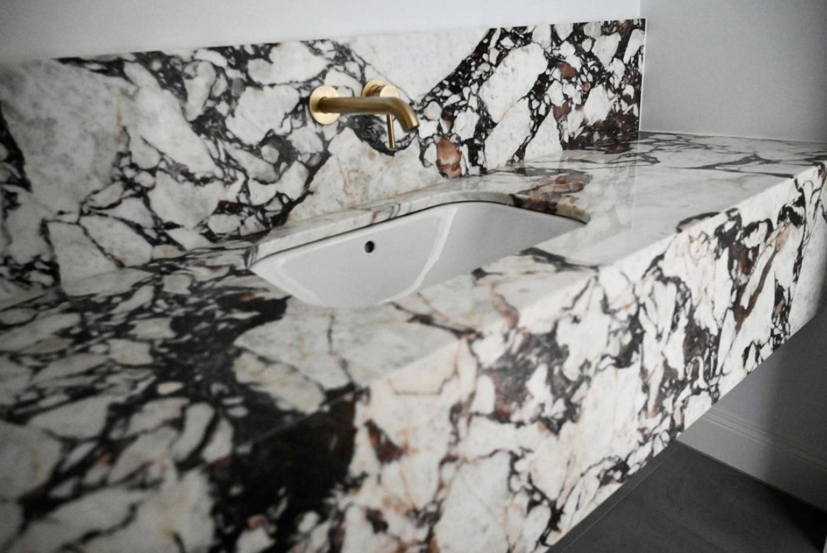 Black-and-white veined stone vanity with an inset basin and brass wall-mounted tap.