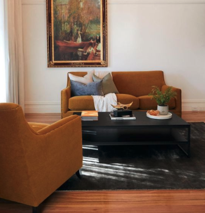 Rust-toned sofa and armchair arranged around a black coffee table beneath a framed painting.