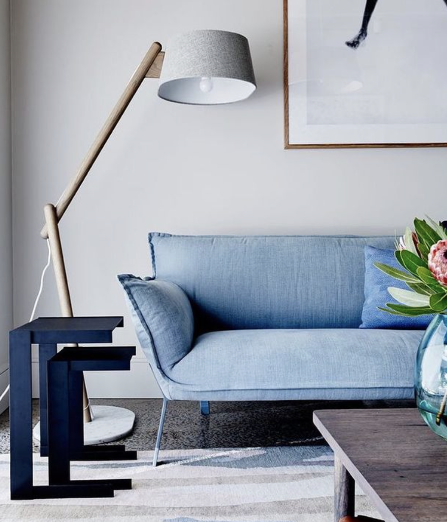 Blue two-seat sofa with a floral cushion and a slender floor lamp.