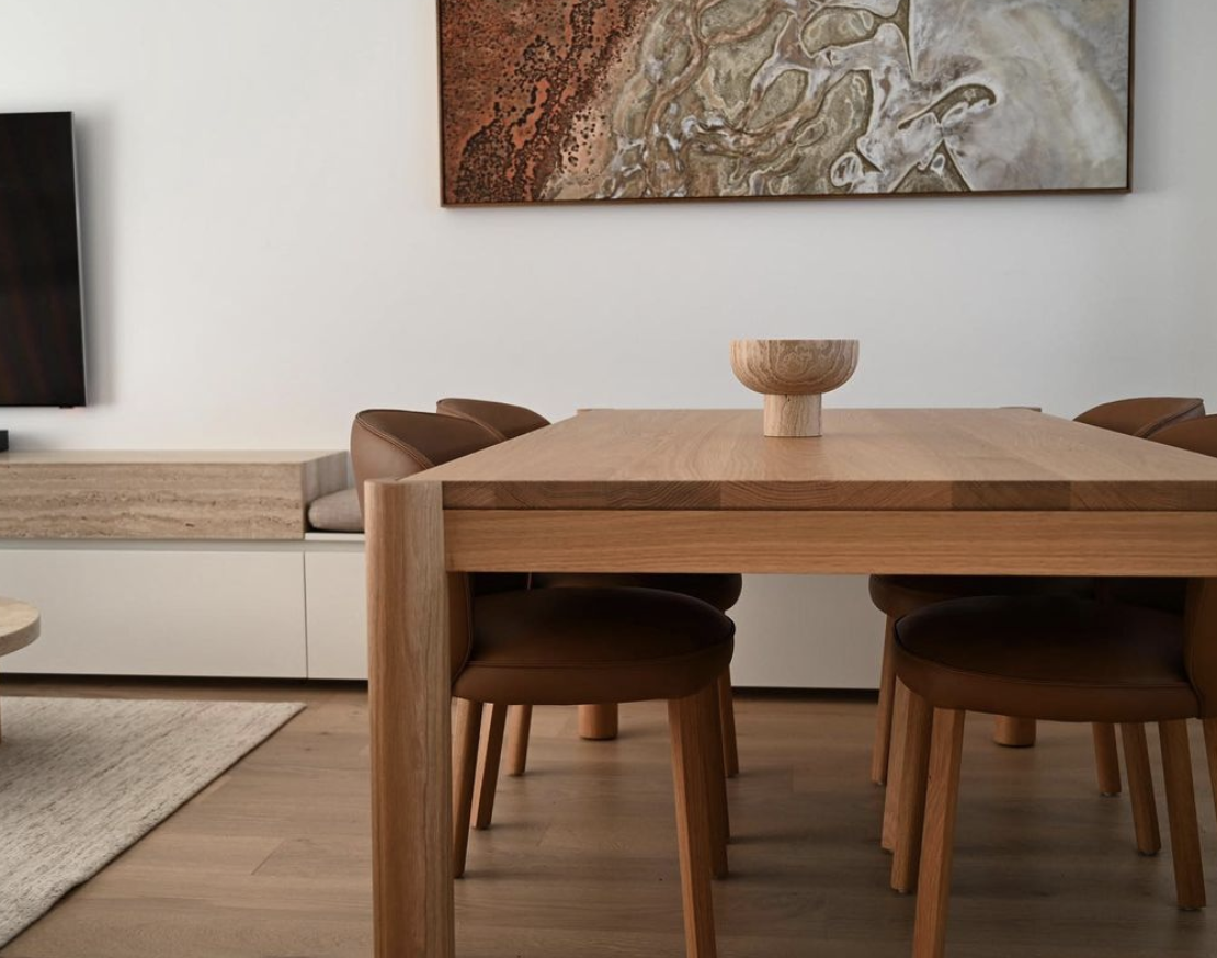 Warm timber dining table and chairs with cream cabinetry and an earthy abstract artwork.