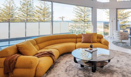 Curving mustard modular sofa with round tables beside a bright window.