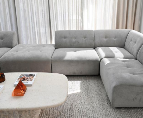 Light grey modular corner sofa beside sheer curtains and a white stone coffee table.