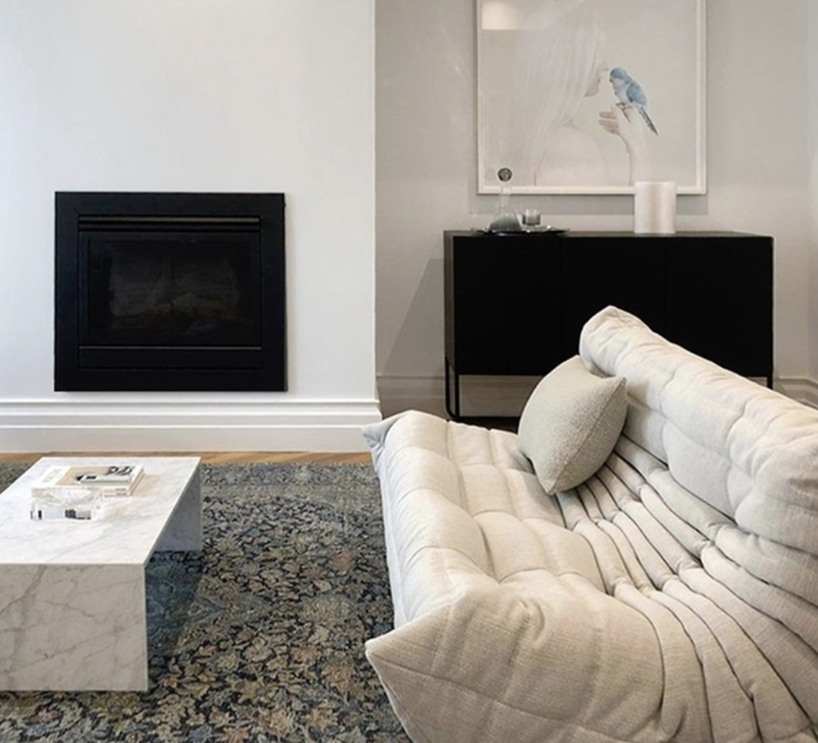 Cream pleated sofa and pale stone coffee table beside a black fireplace.