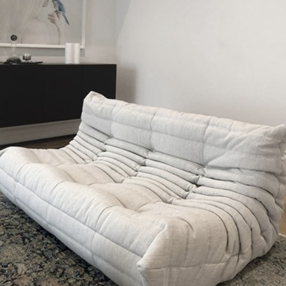Low white sofa with pleated upholstery and generous cushions in a contemporary living room.
