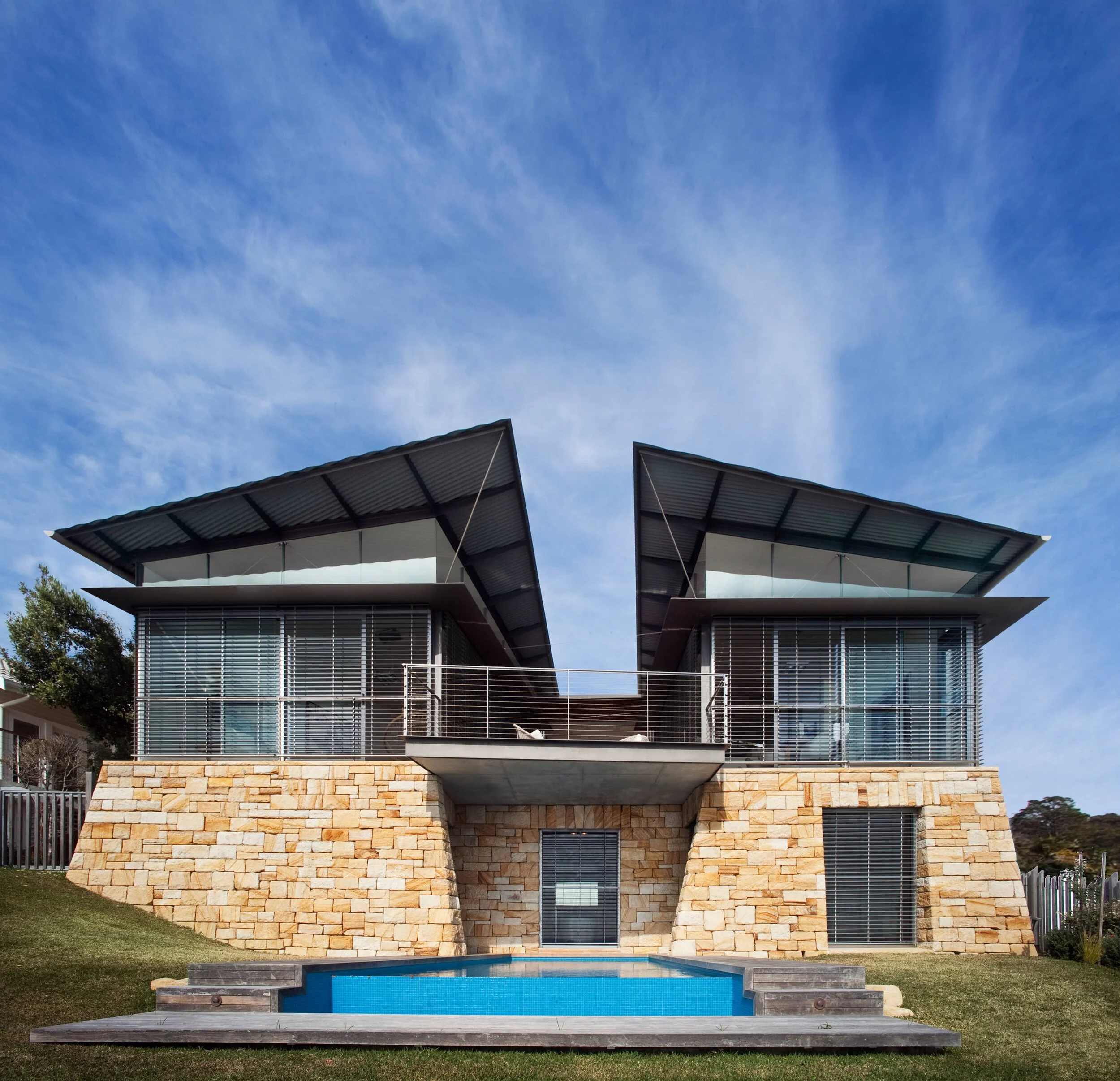Whale Beach House by Casey Brown Architecture, with sandstone walls, twin angular roof forms and a pool.