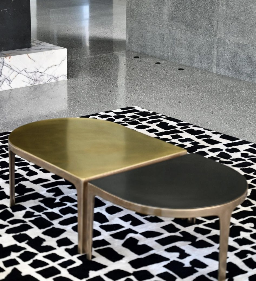 Paired brass-toned and dark coffee tables on a black-and-white patterned rug.