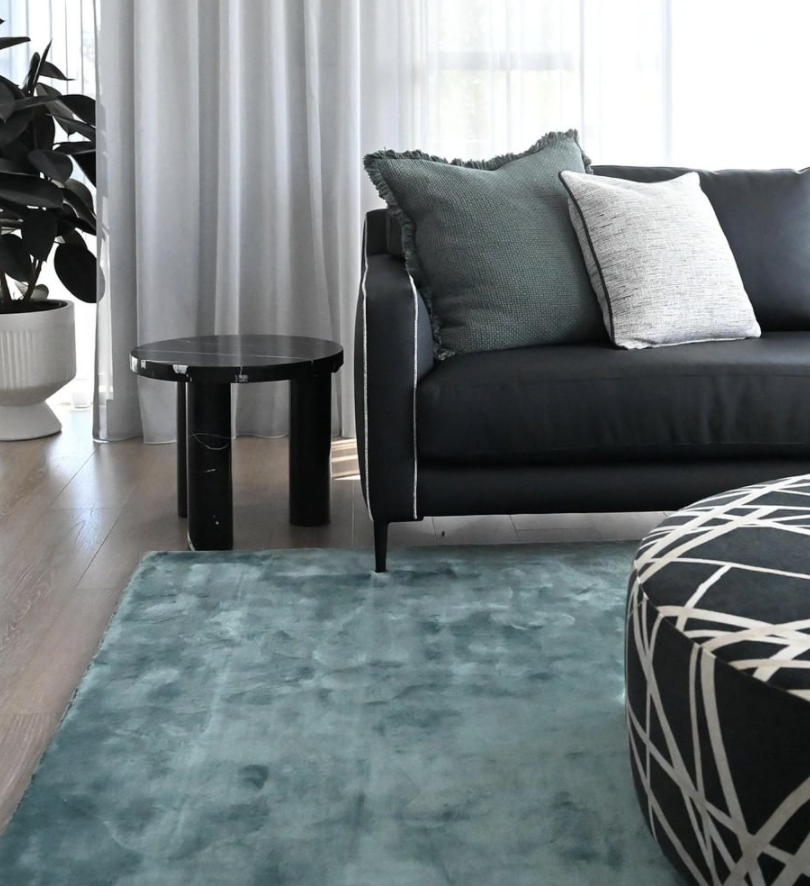 Teal rug, dark sofa and round black side table beside sheer curtains.