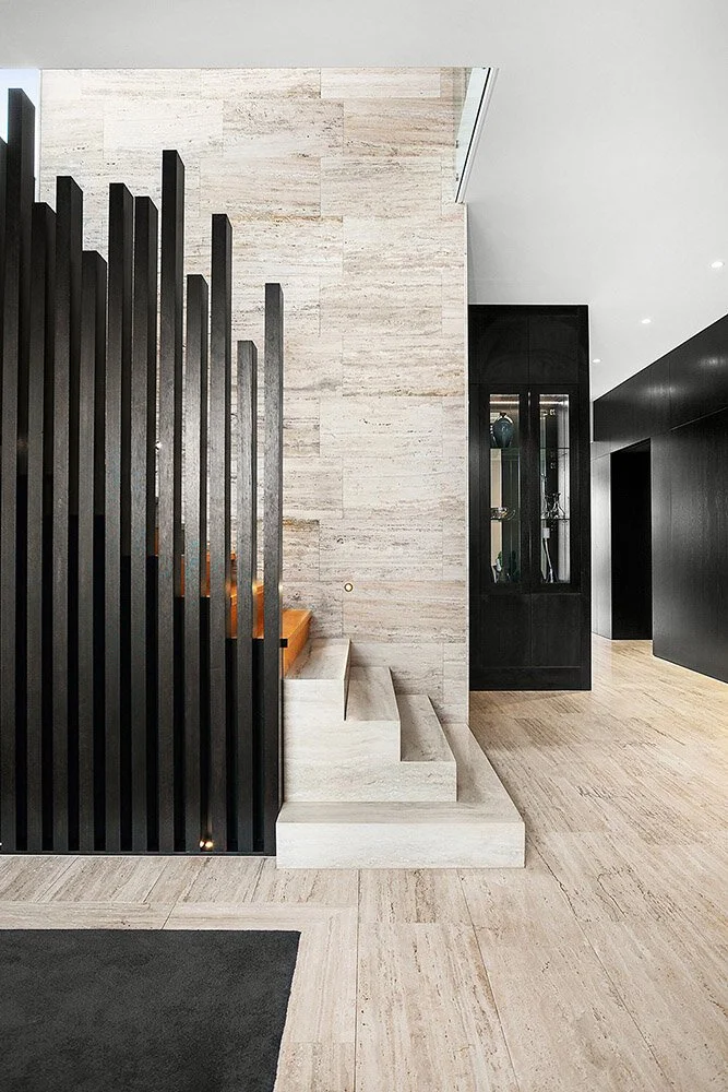 Silver travertine flooring and steps beside a black vertical balustrade and dark joinery.