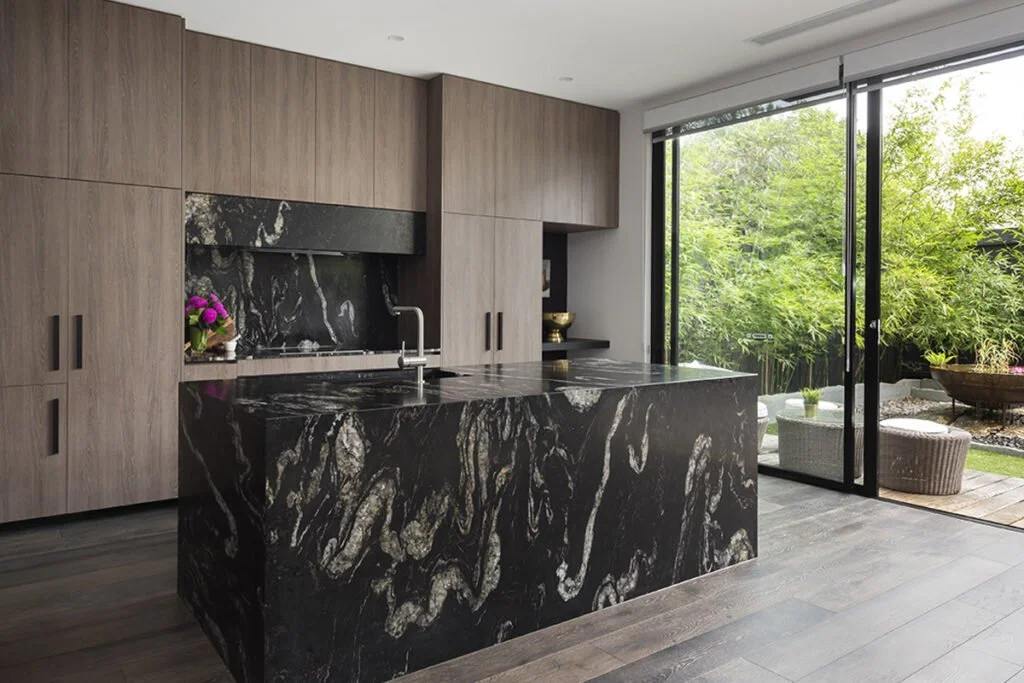 Black granite kitchen island and splashback with pale veining, timber cabinetry and full-height garden glazing.