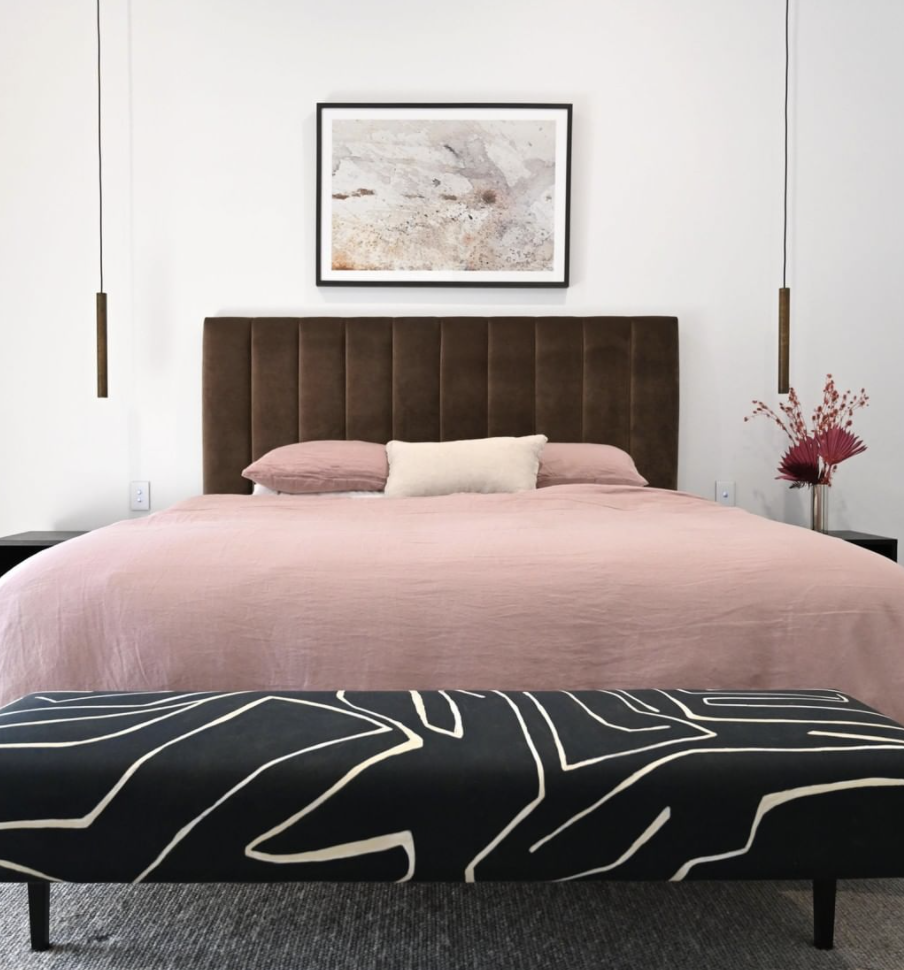 Pink bed linen against a timber bedhead, with a patterned black bench at the foot of the bed.
