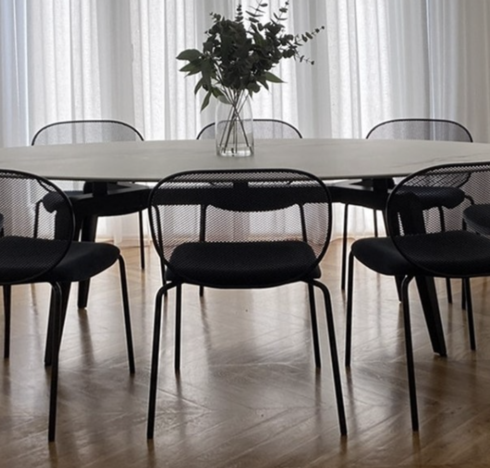 Black dining table and wire-frame chairs beside full-height sheer curtains.