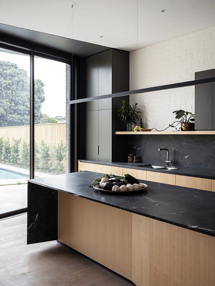 Dark quartzite kitchen island and splashback paired with light timber cabinetry and black-framed glazing.