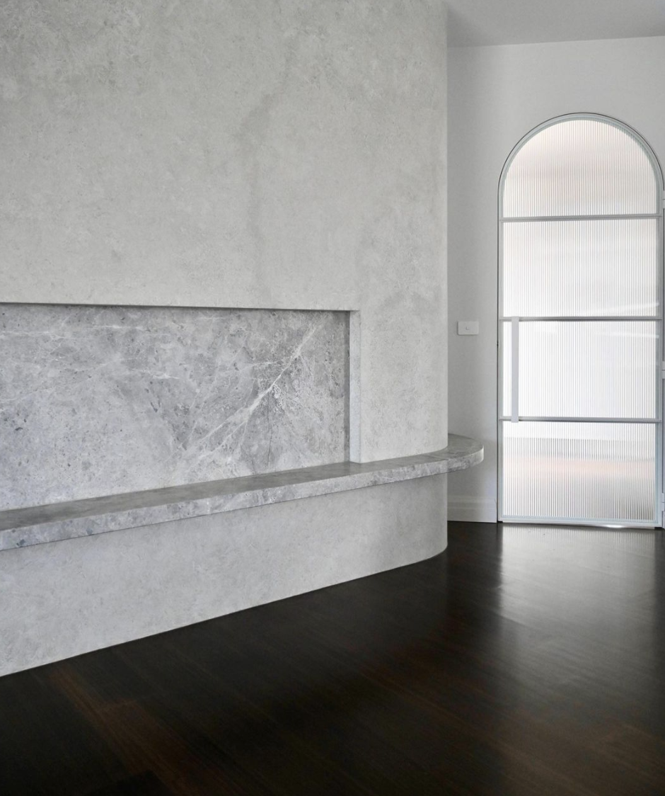 Pale natural-stone fireplace surround beside an arched opening.