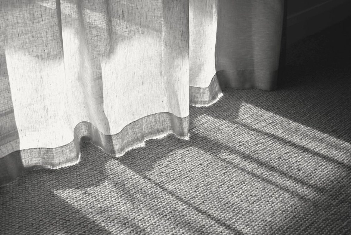 Sunlight through sheer curtains casts patterned shadows across a textured rug.