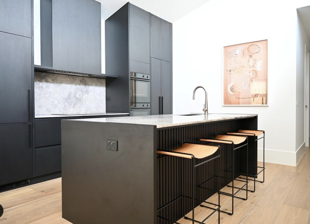 Dark kitchen cabinetry with pale stone splashback, timber island detail and stools.